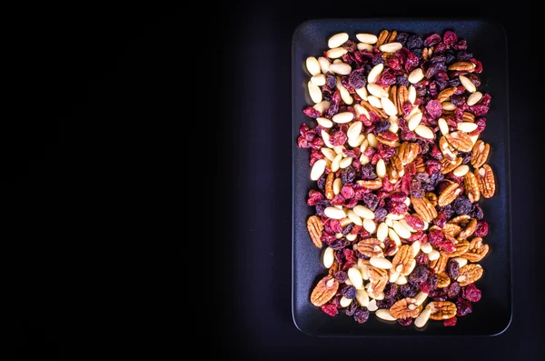 Frutas secas: pacanas, arándanos, pasas, almendras en cuencos de porcelana negra sobre fondo negro. Espacio libre para texto . —  Fotos de Stock