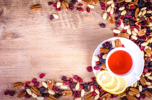 Frutas secas: pacana, arándano, pasas, almendra con taza de té blanco sobre fondo de madera. Espacio libre para texto . —  Fotos de Stock