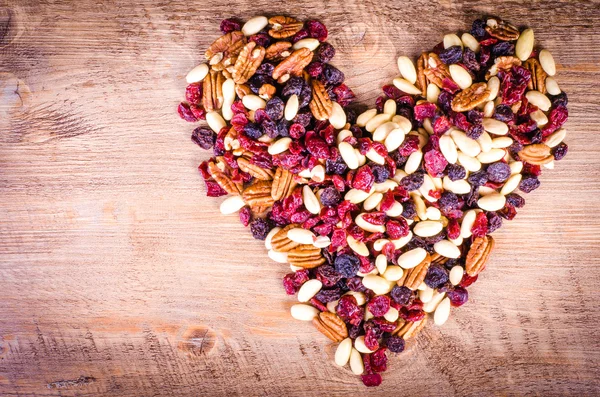 Las frutas secas - la pacana, el arándano, las pasas, la almendra que forman el corazón sobre el fondo de madera. Espacio libre para texto . —  Fotos de Stock