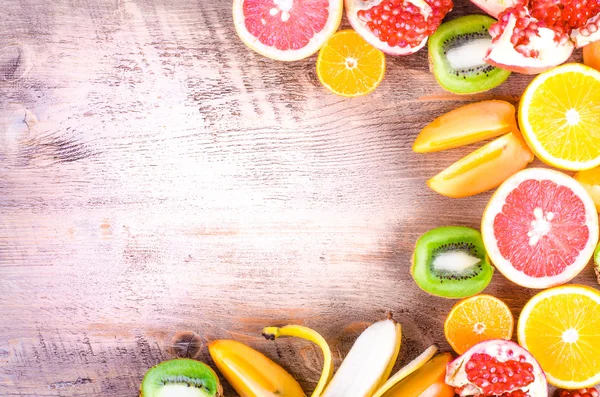 Fresh fruits on wooden background. Summer background. Raw and vegetarian eating frame. Sliced orange, persimmon, kiwi, tangerine, banana, lemon, apple,  grapefruit, pomegranate, lime,  Top view — Stockfoto