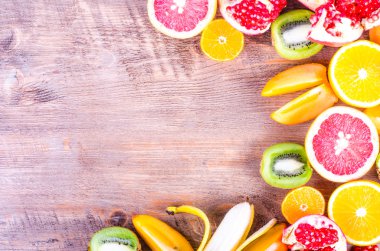 Fresh fruits on wooden background. Summer background. Raw and vegetarian eating frame. Sliced orange, persimmon, kiwi, tangerine, banana, lemon, apple,  grapefruit, pomegranate, lime,  Top view