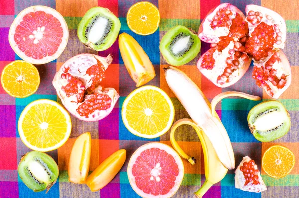 Frutas frescas en una toalla de cocina a cuadros de colores. Raw y vegetariano comer fondo. Naranja en rodajas, caqui, kiwi, mandarina, plátano, limón, manzana, pomelo, granada, lima, Vista superior — Foto de Stock