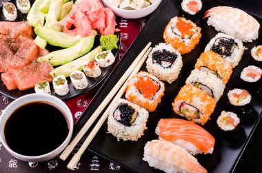 Sushi set, soy sauce, ginger, wasabi, black and red roe, avocado, salmon, cheese on black background 