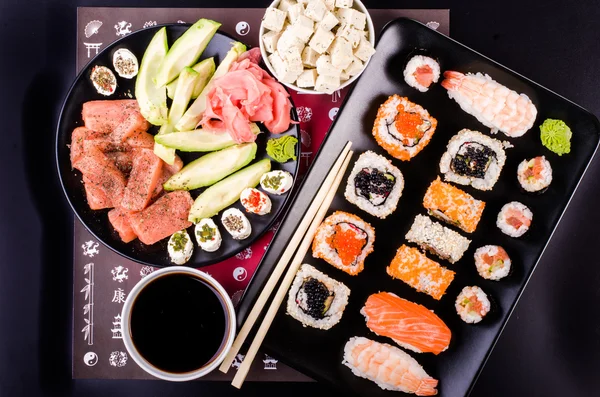 Sushi set, soy sauce, ginger, wasabi, black and red roe, avocado, salmon, cheese on black background — Stock fotografie