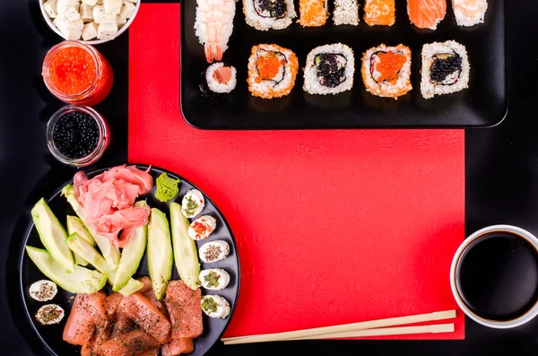 Sushi set, soy sauce, ginger, wasabi, black and red roe, avocado, salmon, cheese on black and red background. Free space for your text — ストック写真