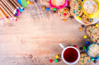 Fresh homemade muffins and cookies with color chocolate coated candies, colorful wooden pencils, cup of tea on a rustic background. Free space for your text