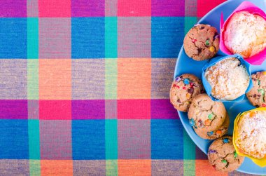 Fresh homemade muffins and cookies with color chocolate coated candies on a colorful checkered kitchen towel. Free space for your text