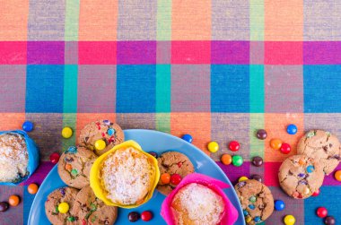 Fresh homemade muffins and cookies with color chocolate coated candies on a colorful checkered kitchen towel. Free space for your text