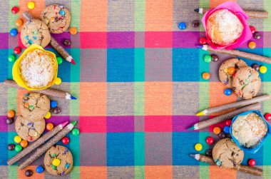 Fresh homemade muffins and cookies with color chocolate coated candies, colorful wooden pencils on a checkered kitchen towel. Free space for your text