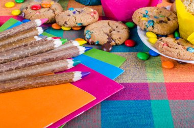 Fresh homemade muffins and cookies with color chocolate coated candies, colorful wooden pencils on a checkered kitchen towel. Free space for your text