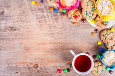 Fresh homemade muffins and cookies with color chocolate coated candies, cup of tea wooden background. Free space for your text