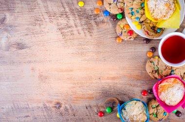 Fresh homemade muffins and cookies with color chocolate coated candies, cup of tea wooden background. Free space for your text