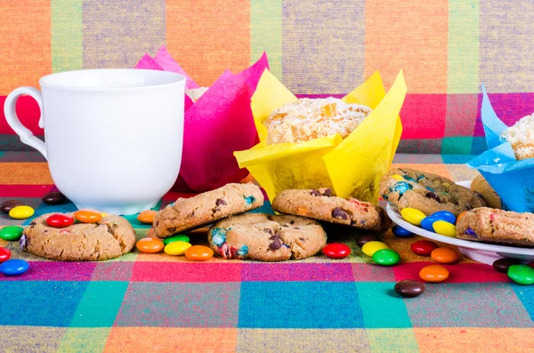 Muffins frais faits maison et biscuits avec des bonbons enrobés de chocolat de couleur, tasse de thé sur une serviette de cuisine colorée à carreaux. Espace libre pour votre texte — Photo