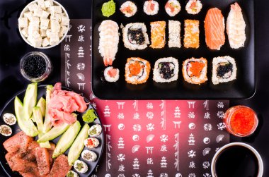 Sushi set, soy sauce, ginger, wasabi, black and red roe, avocado, salmon, cheese on black background with Japanese characters
