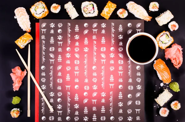 Набор суши, соевый соус, имбирь, васаби на черном фоне с японскими символами — стоковое фото