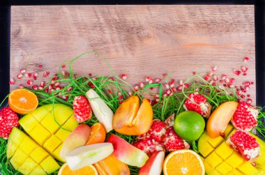 Fresh fruits on grass and wooden background. Raw and vegetarian eating frame. Sliced orange, persimmon, kiwi, tangerine, banana, lemon, apple,  grapefruit, pomegranate, lime, mango. Fruit set.