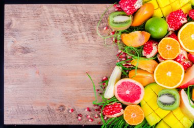 Fresh fruits on grass and wooden background. Raw and vegetarian eating frame. Sliced orange, persimmon, kiwi, tangerine, banana, lemon, apple,  grapefruit, pomegranate, lime, mango. Fruit set.
