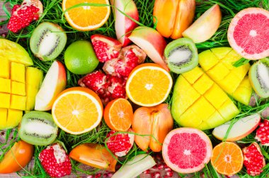 Fresh fruits on grass and wooden background. Raw and vegetarian eating frame. Sliced orange, persimmon, kiwi, tangerine, banana, lemon, apple,  grapefruit, pomegranate, lime, mango. Fruit set.