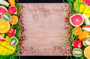 Fresh fruits on grass and wooden background. Raw and vegetarian eating frame. Sliced orange, persimmon, kiwi, tangerine, banana, lemon, apple,  grapefruit, pomegranate, lime, mango. Fruit set.