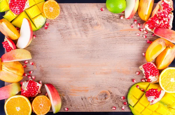 Fresh fruits on a wooden background. Raw and vegetarian eating frame. Sliced orange, persimmon, kiwi, tangerine, banana, lemon, apple,  grapefruit, pomegranate, lime, mango. Fruit set.