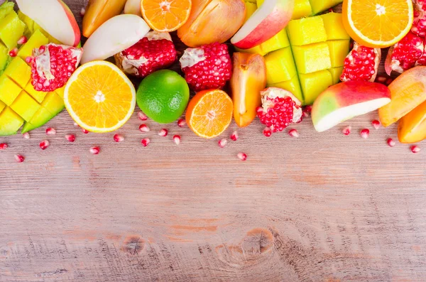 Frutas frescas sobre un fondo de madera. Marco alimenticio crudo y vegetariano. Naranja en rodajas, caqui, kiwi, mandarina, plátano, limón, manzana, pomelo, granada, lima, mango. Conjunto de frutas . —  Fotos de Stock