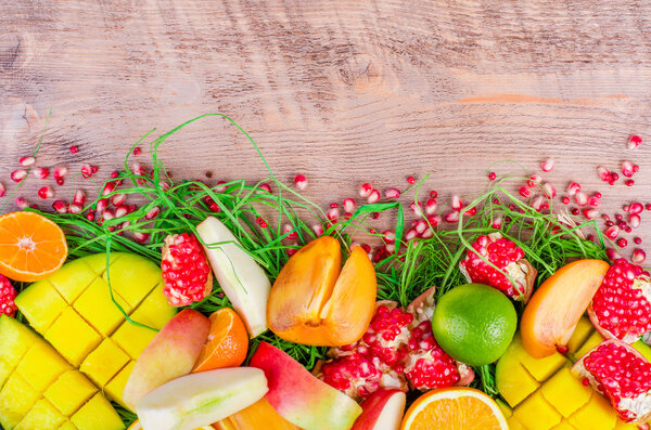 Fresh fruits on grass and wooden background. Raw and vegetarian eating frame. Sliced orange, persimmon, kiwi, tangerine, banana, lemon, apple,  grapefruit, pomegranate, lime, mango. Fruit set.