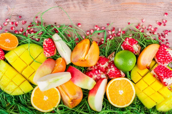 Fresh fruits on grass and wooden background. Raw and vegetarian eating frame. Sliced orange, persimmon, kiwi, tangerine, banana, lemon, apple,  grapefruit, pomegranate, lime, mango. Fruit set.