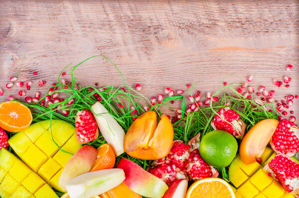 Fresh fruits on grass and wooden background. Raw and vegetarian eating frame. Sliced orange, persimmon, kiwi, tangerine, banana, lemon, apple,  grapefruit, pomegranate, lime, mango. Fruit set.