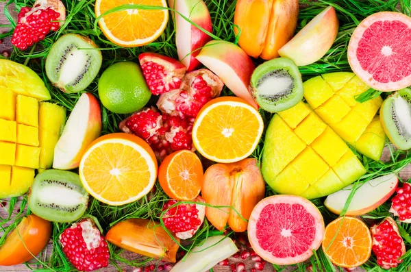 Fresh fruits on grass and wooden background. Raw and vegetarian eating frame. Sliced orange, persimmon, kiwi, tangerine, banana, lemon, apple,  grapefruit, pomegranate, lime, mango. Fruit set.