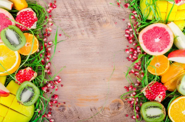 Fresh fruits on grass and wooden background. Raw and vegetarian eating frame. Sliced orange, persimmon, kiwi, tangerine, banana, lemon, apple,  grapefruit, pomegranate, lime, mango. Fruit set.