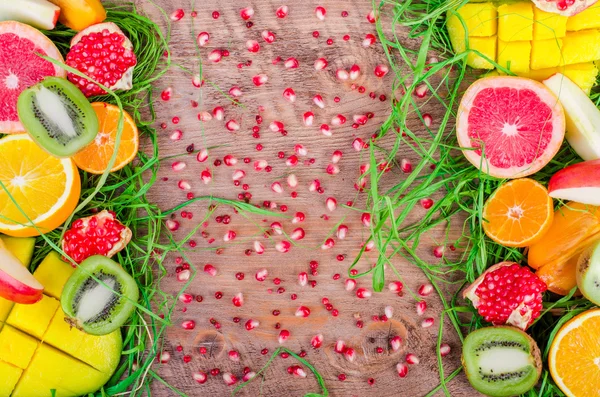 Fresh fruits on grass and wooden background. Raw and vegetarian eating frame. Sliced orange, persimmon, kiwi, tangerine, banana, lemon, apple,  grapefruit, pomegranate, lime, mango. Fruit set.