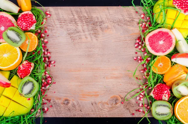 Fresh fruits on grass and wooden background. Raw and vegetarian eating frame. Sliced orange, persimmon, kiwi, tangerine, banana, lemon, apple,  grapefruit, pomegranate, lime, mango. Fruit set.