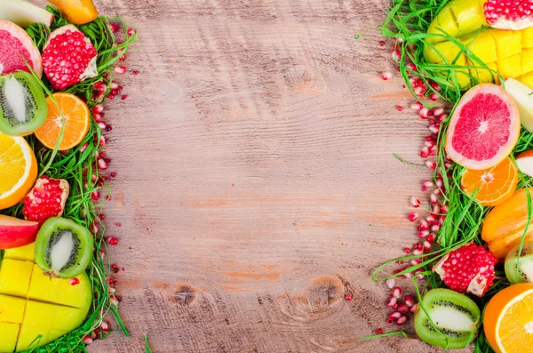 Fresh fruits on grass and wooden background. Raw and vegetarian eating frame. Sliced orange, persimmon, kiwi, tangerine, banana, lemon, apple,  grapefruit, pomegranate, lime, mango. Fruit set.