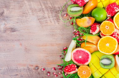 Fresh fruits on a wooden background. Raw and vegetarian eating frame. Sliced orange, persimmon, kiwi, tangerine, banana, lemon, apple,  grapefruit, pomegranate, lime, mango. Fruit set.