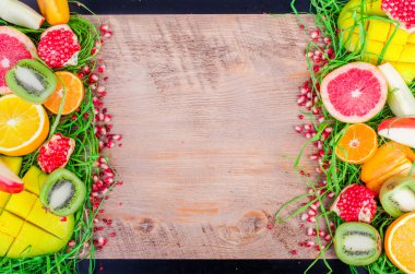 Fresh fruits on grass and wooden background. Raw and vegetarian eating frame. Sliced orange, persimmon, kiwi, tangerine, banana, lemon, apple,  grapefruit, pomegranate, lime, mango. Fruit set.
