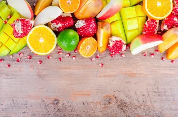 Frutas frescas sobre un fondo de madera. Marco alimenticio crudo y vegetariano. Naranja en rodajas, caqui, kiwi, mandarina, plátano, limón, manzana, pomelo, granada, lima, mango. Conjunto de frutas . —  Fotos de Stock