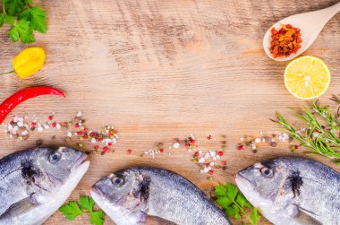 Fresh raw gilthead fishes with lemon, herbs, olive oil, salt on wooden background. Healthy food concept. Food frame