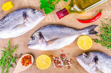 Fresh raw gilthead fishes with lemon, herbs, olive oil, salt on wooden background. Healthy food concept. Food frame