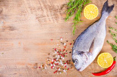 Fresh raw gilthead fishes with lemon, herbs, salt on wooden background. Healthy food concept. Food frame