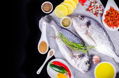 Fresh raw gilthead fishes with lemon, herbs, salt on black background. Healthy food concept. Food frame