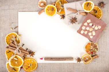Dried oranges, cinnamon, cloves, cardamom, handmade milk chocolate with nuts, wooden pencil, list of paper on sackcloth, canvas. Christmas, New Year and winter. Free space for your text.
