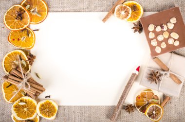 Dried oranges, cinnamon, cloves, cardamom, handmade milk chocolate with nuts, wooden pencil, list of paper on sackcloth, canvas. Christmas, New Year and winter. Free space for your text.
