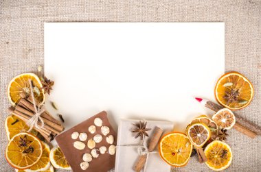 Dried oranges, cinnamon, cloves, cardamom, handmade milk chocolate with nuts, wooden pencil, list of paper on sackcloth, canvas. Christmas, New Year and winter. Free space for your text.