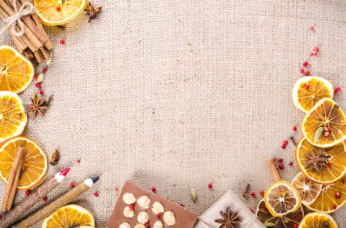 Dried oranges, cinnamon, cloves, cardamom, handmade milk chocolate with nuts, wooden pencil, list of paper on sackcloth, canvas. Christmas, New Year and winter. Free space for your text.