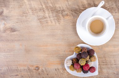 Handmade chocolate candies on plate forming heart and cup of coffee, wooden background. Free space for your text.