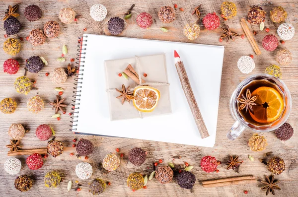 Handmade chocolate candies collection, dried oranges, cinnamon, cloves, cardamom, mulled wine, notebook and pencil on wooden background. Free space for your text. — ストック写真