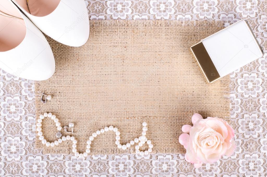 Beautiful set of women's wedding accessories. Bride's morning. White shoes, perfume, pearl necklace and earrings on white lace cloth and sackcloth, canvas.