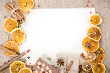 Dried oranges, cinnamon, cloves, cardamom, handmade milk chocolate with nuts, wooden pencil, list of paper on sackcloth, canvas. Christmas, New Year and winter. Free space for your text.