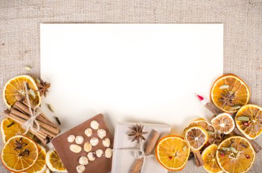 Dried oranges, cinnamon, cloves, cardamom, handmade milk chocolate with nuts, wooden pencil, list of paper on sackcloth, canvas. Christmas, New Year and winter. Free space for your text.