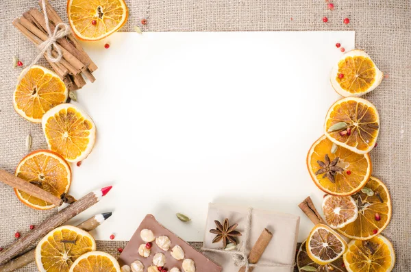 Dried oranges, cinnamon, cloves, cardamom, handmade milk chocolate with nuts, wooden pencil, list of paper on sackcloth, canvas. Christmas, New Year and winter. Free space for your text.